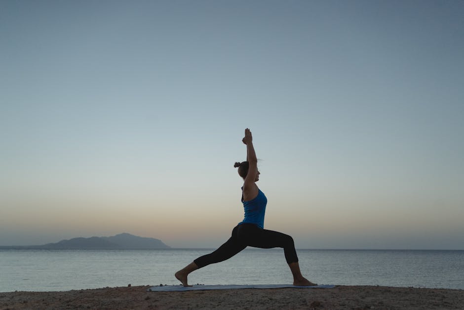 A focused woman stretching in a yoga pose by the ocean at sunrise.